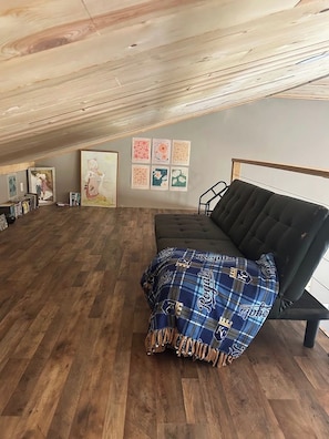 Ein Loft-Zimmer mit schwarzem Sofa, Holzboden und Kunstwerken an den Wänden.