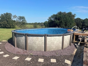 A circular above-ground swimming pool with a ladder, surrounded by a pebble border and a wooden deck.