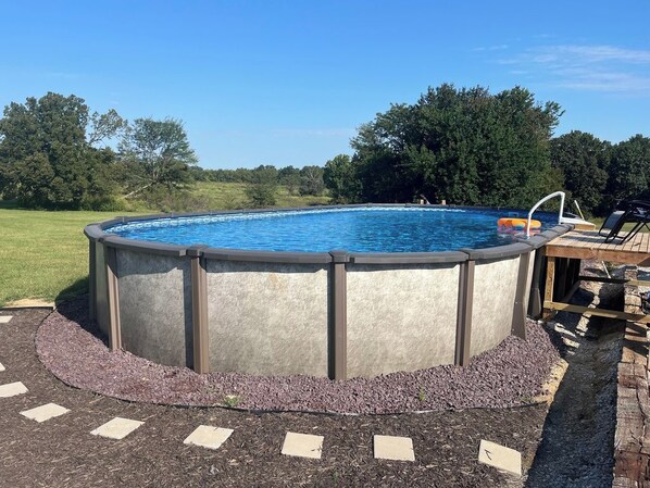 A circular above-ground swimming pool with a ladder, surrounded by a pebble border and a wooden deck.