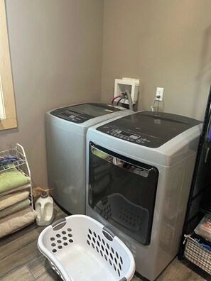 A laundry room with two front-loading washing machines, a white laundry basket, and a milk jug.