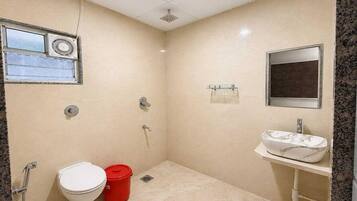 Un baño pequeño con inodoro, un cubo de basura rojo, lavamanos y espejo.