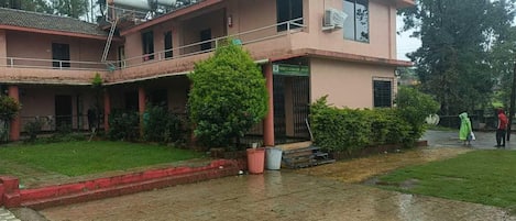 Un edificio de dos pisos con techo plano, un vestíbulo cubierto y un pequeño jardín con césped y plantas en macetas.
