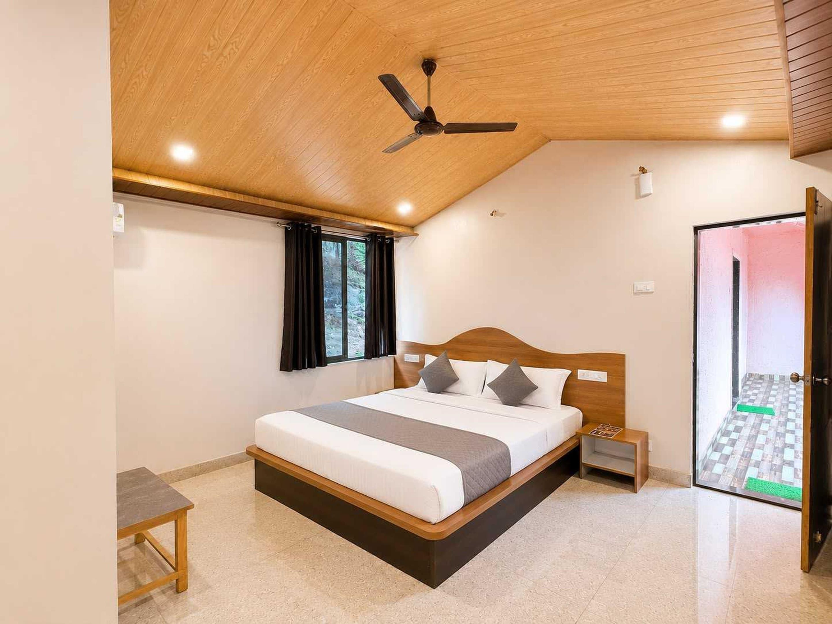 A bedroom with a sloped ceiling, a bed with a wooden headboard, a nightstand, a table, and a window with curtains.