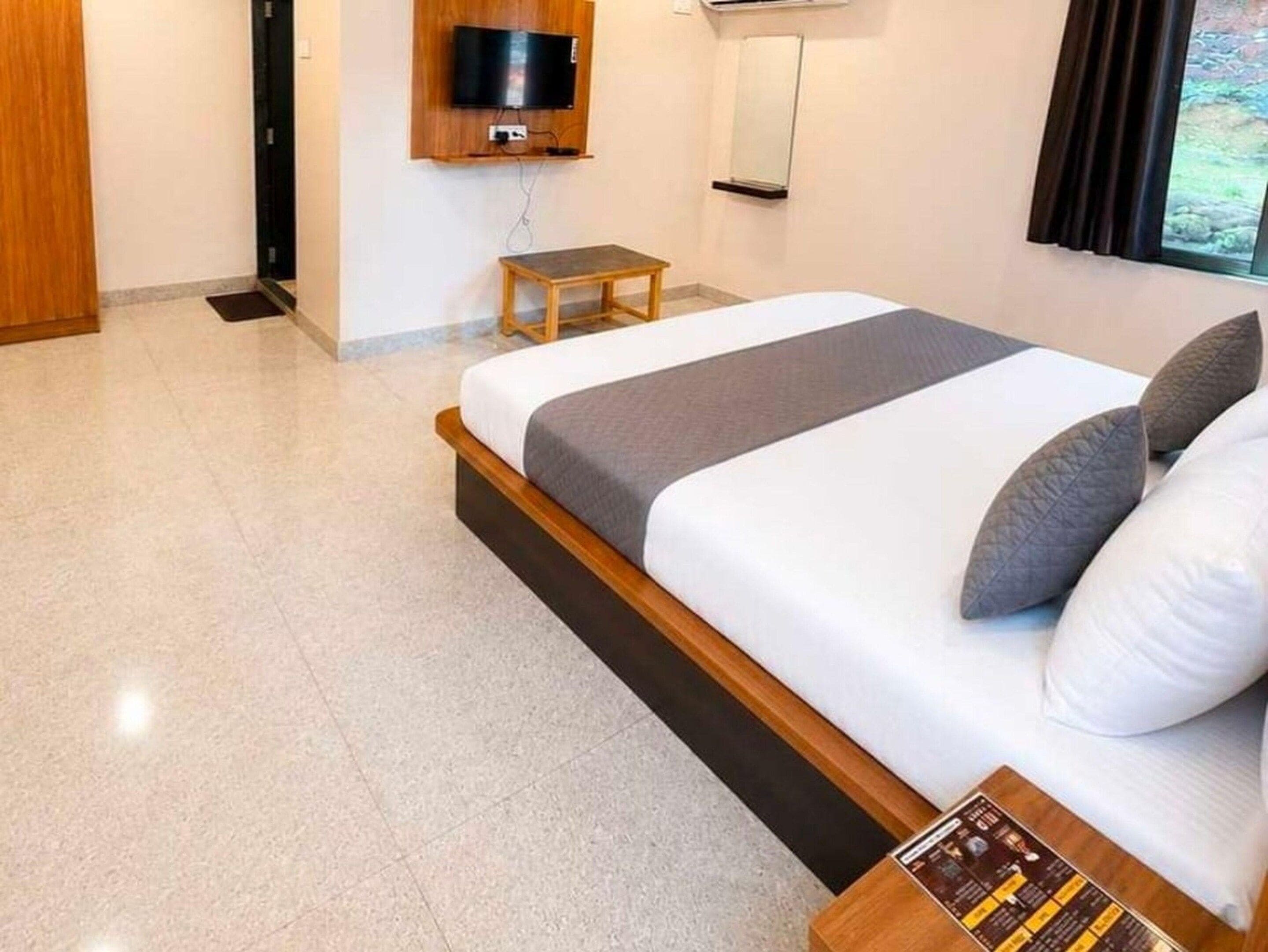 Een moderne slaapkamer met een bed, een klein tafeltje, een televisie en een raam.