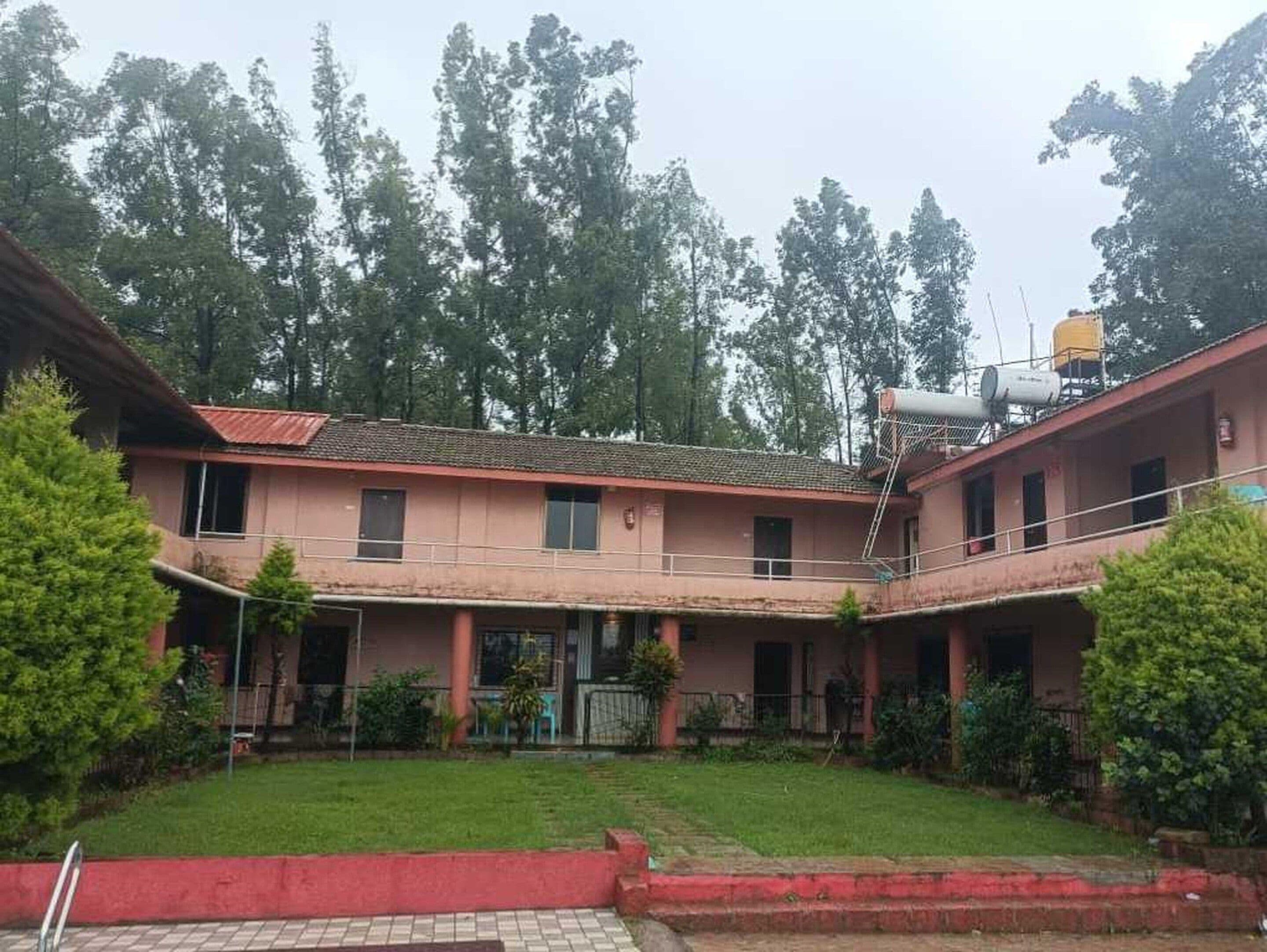 A two-story building with a flat roof, a water tank on the roof, and a small garden area in front.