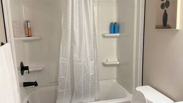 A modern bathroom with a bathtub, toilet, and shower curtain.