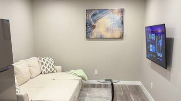 A modern living room with a sofa, a coffee table, a flat-screen TV mounted on the wall, and a decorative painting above the sofa.