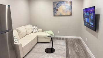 A modern living room with a sectional sofa, a flat-screen TV mounted on the wall, and a small round table.