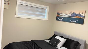 A bedroom with a bed, a nightstand, a window with blinds, a painting, and a ceiling light.