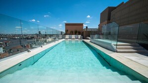 Una piscina en la azotea con agua azul cristalina, rodeada de barandillas de vidrio y vistas a la ciudad.