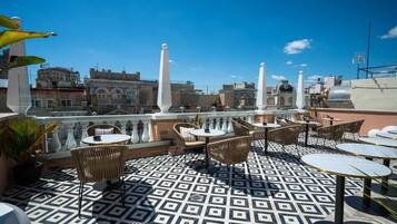 Terraza en la azotea con suelo estampado, mobiliario exterior y vistas a la ciudad.