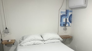 Ein Bett mit weißer Bettwäsche, eine Wand-Klimaanlage und eine hängende Leuchte.