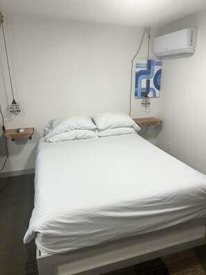 Ein Bett mit weißer Bettwäsche, eine Wand-Klimaanlage und eine hängende Leuchte.