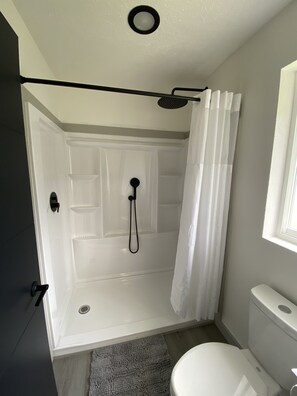 A bathroom with a shower, toilet, and a door leading to another room. - 2 Queen Beds Near Silverwood Theme Park | Room 7 (Athol)