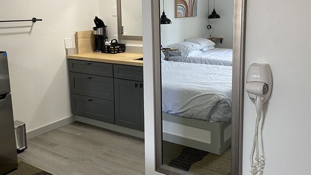 Hotellihuone, jossa on sänky, lipasto, peili, hiustenkuivaaja ja pieni keittonurkkaus.