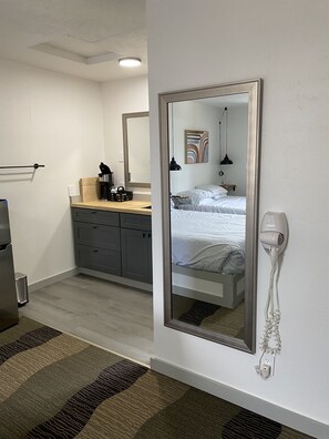 Una habitación de hotel con cama, cómoda, espejo, secador de pelo y una pequeña cocina.