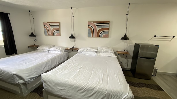 Hotellihuone, jossa on kaksi sänkyä, jääkaappi ja taideteoksia seinillä.