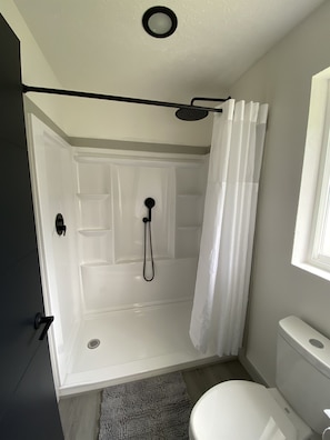 A bathroom with a shower, toilet, and a door leading to another room. - 2 Queen Beds Near Silverwood Theme Park | Room 8 (Athol)