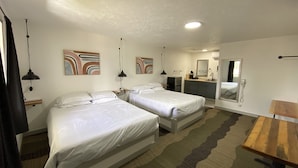 Hotellihuone, jossa on kaksi sänkyä, työpöytä, peili ja taustalla näkyvä kylpyhuone.