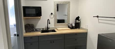 Cocina compacta con microondas integrado, lavamanos y cafetera.