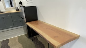 Huoneessa on puinen penkki, harmailla kaapeilla varustettu keittiö sekä kuvioitu matto.