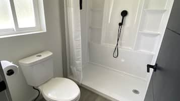 A bathroom with a toilet, a shower with a handheld showerhead, and a window.