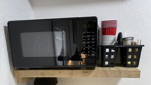 Et køkken med en mikrobølgeovn, kaffemaskine og en stabel røde og hvide tallerkener på en hylde.