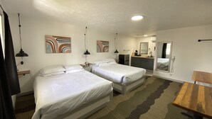 Et hotelværelse med to senge, et skrivebord, et spejl og et badeværelse i baggrunden.