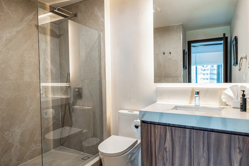 A modern bathroom with a glass-enclosed shower, a white toilet, and a vanity with a mirror.