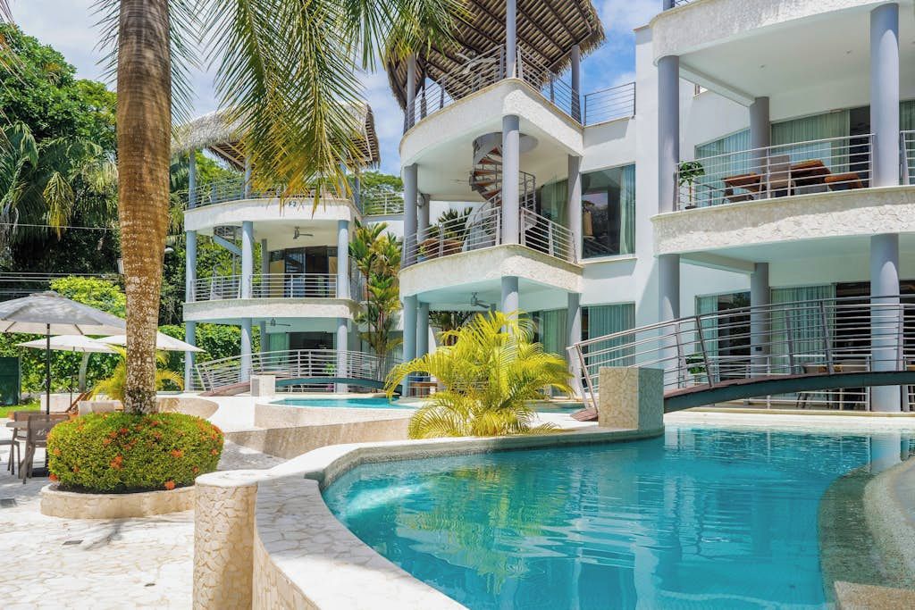 A multi-story hotel with a swimming pool, outdoor seating, and lush greenery.