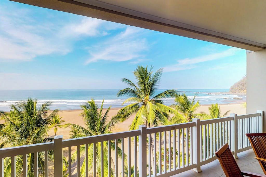 A balcony with a view of a beach and palm trees.