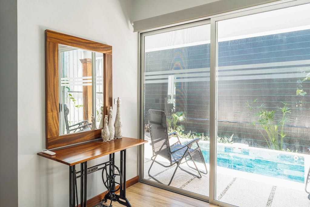 Una habitación con una consola de madera, una máquina de coser y un amplio ventanal corredero que da a una zona de piscina.