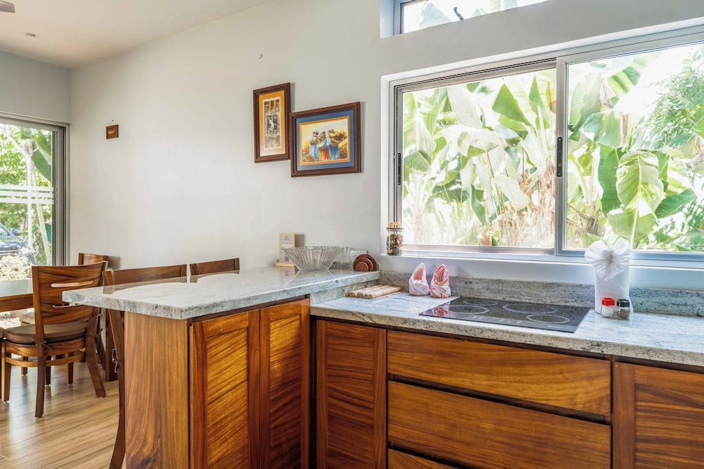 A kitchen with wooden cabinets, a marble countertop, and a window with a view of greenery.