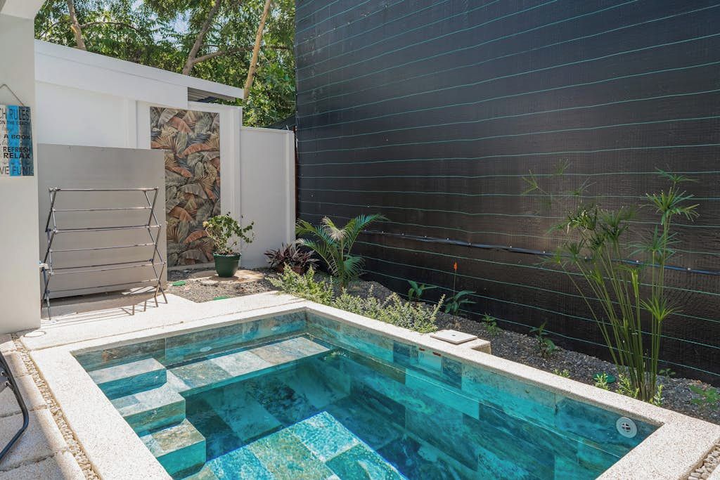 A swimming pool with a stone border, a metal drying rack, and a potted plant.