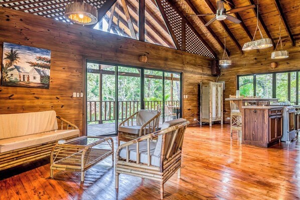 Un intérieur spacieux en bois, avec un plafond haut, de grandes fenêtres et un espace salon central comprenant un canapé et des fauteuils.