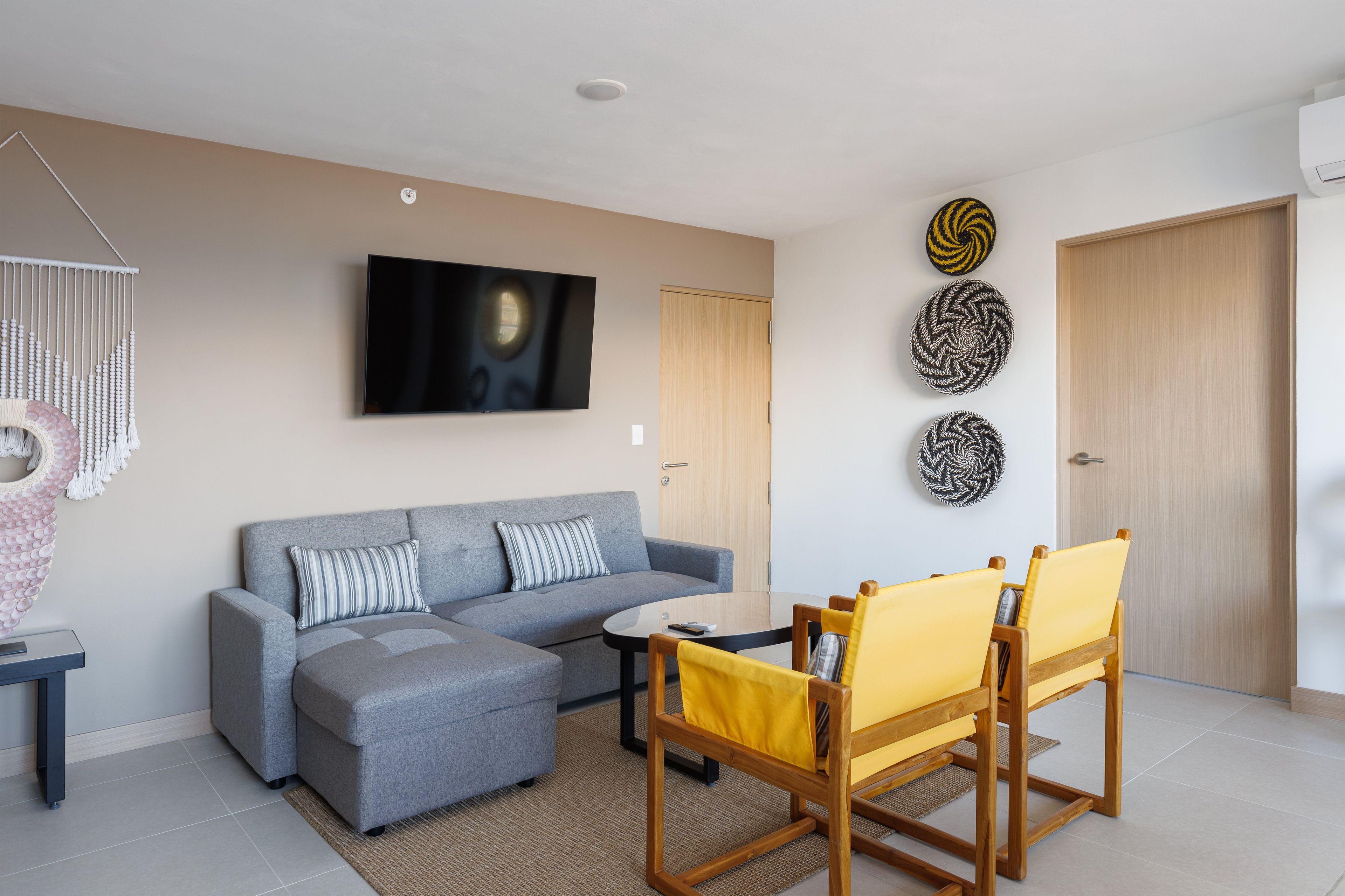 A modern living room with a grey sectional sofa, a round coffee table, and yellow chairs.