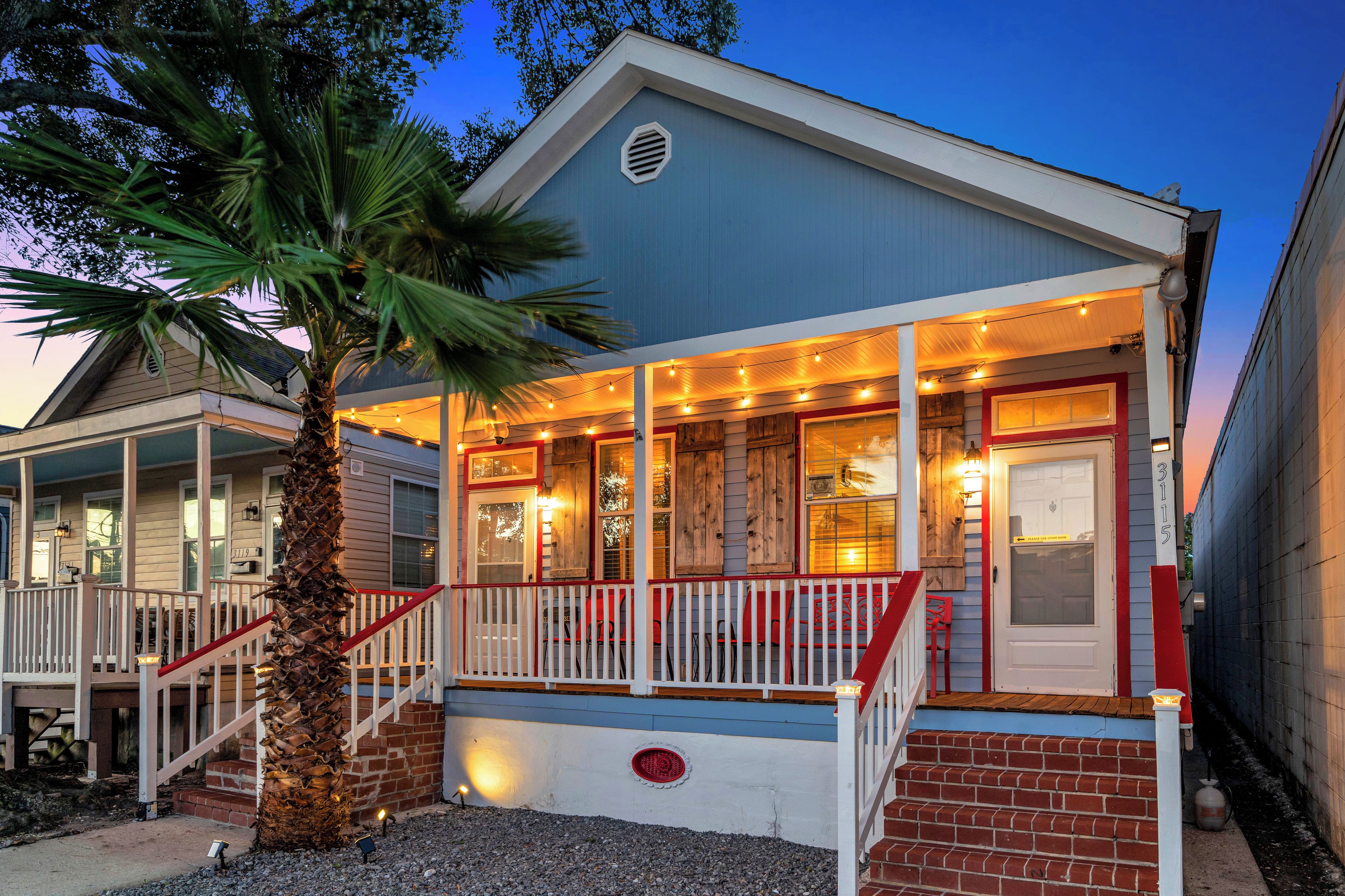 A two-story house with a porch, a palm tree, and a brick foundation.