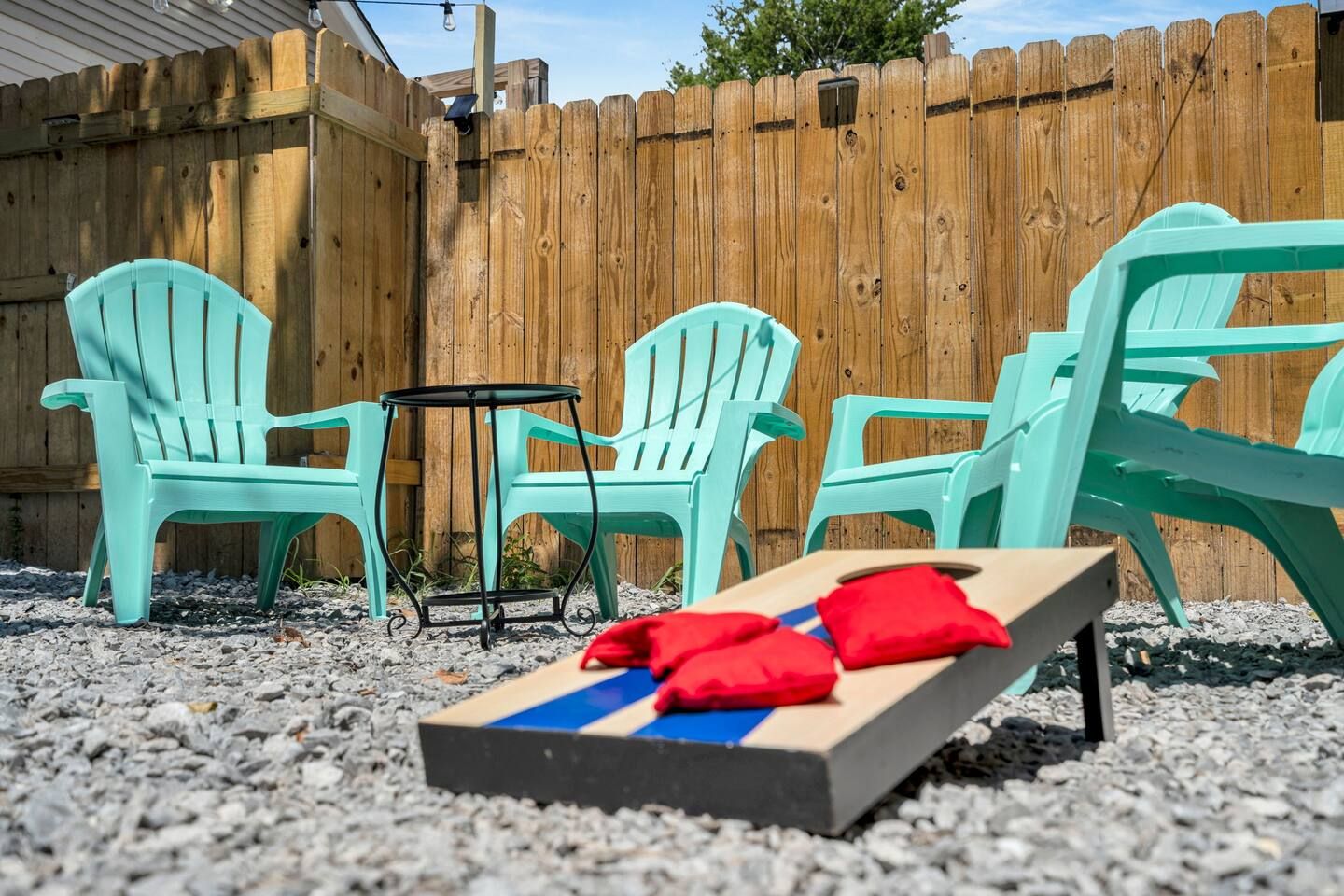 Un patio con dos sillas turquesas, una mesita redonda y una mesa para juego de rifa con discos rojos.