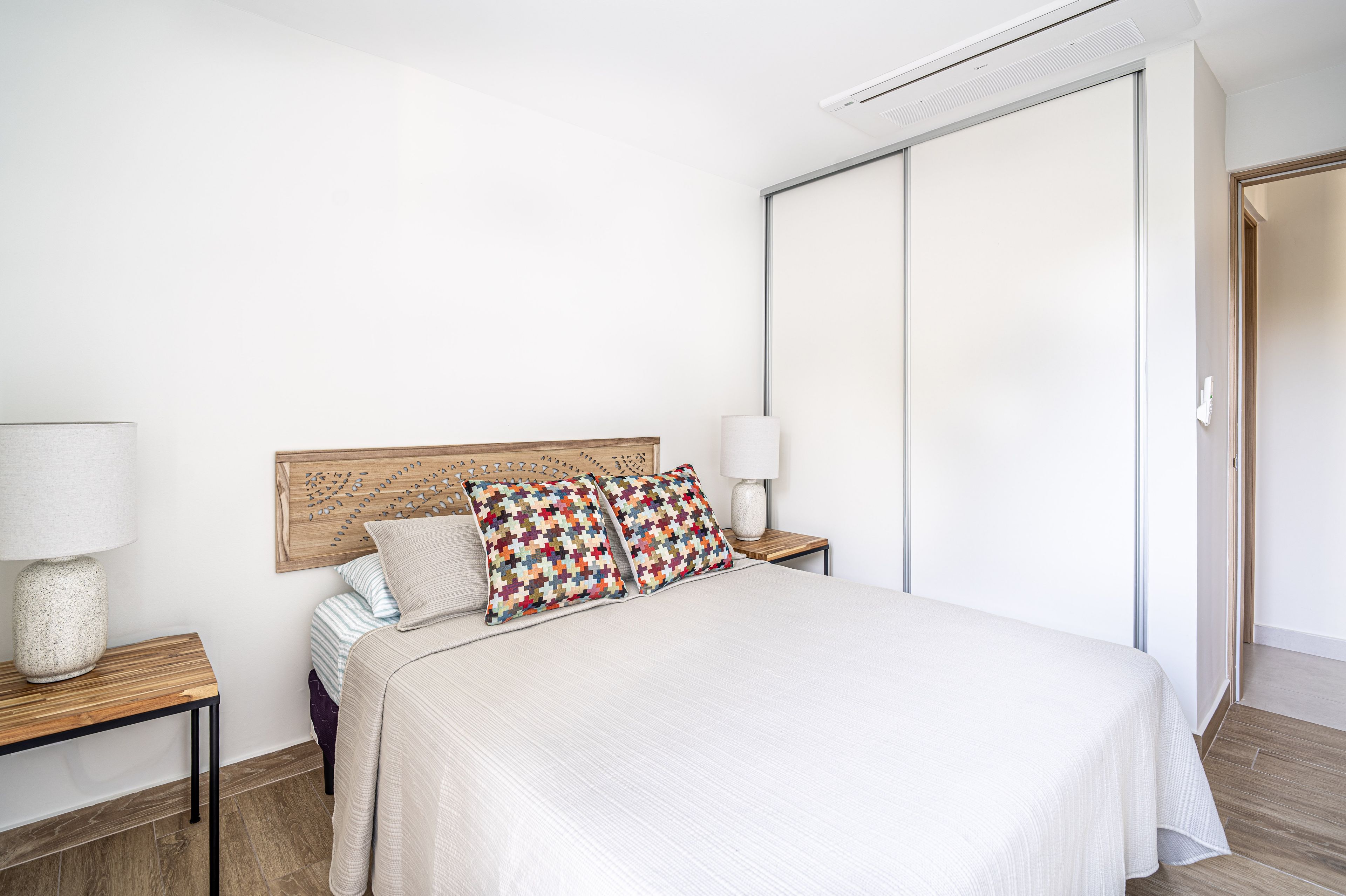 A neatly made bed with a headboard, two bedside tables with lamps, and a large closet.