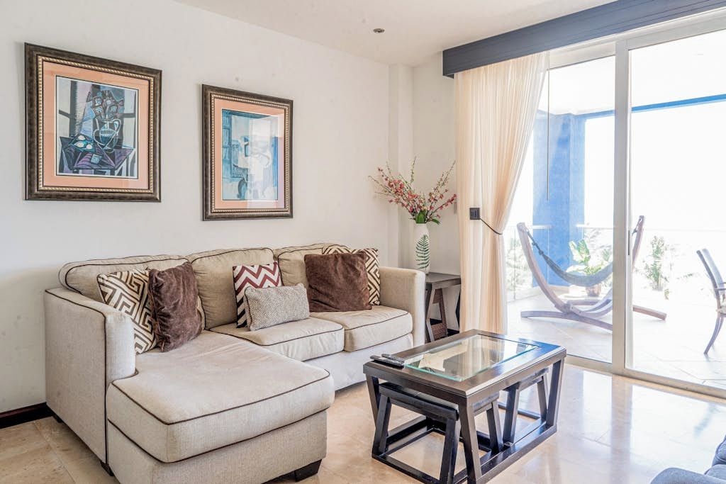A living room with a sofa, a glass coffee table, and two framed artworks on the wall.