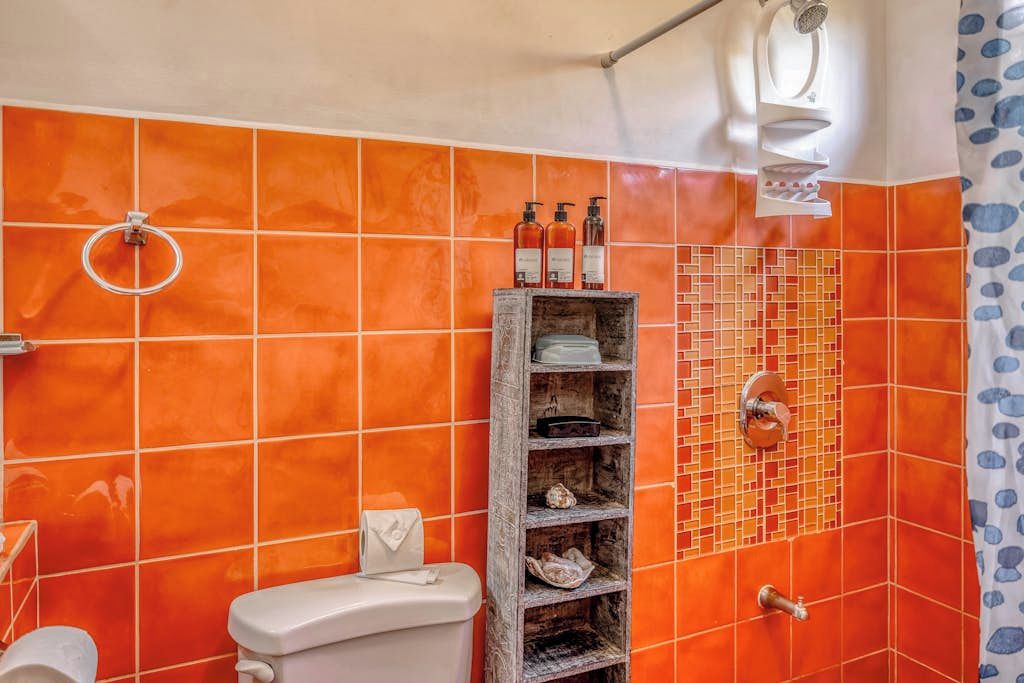 Ein Badezimmer mit orangefarbenen Fliesen, einer Toilette, einem Ablagefach für Pflegeprodukte und einer Duschkabine.