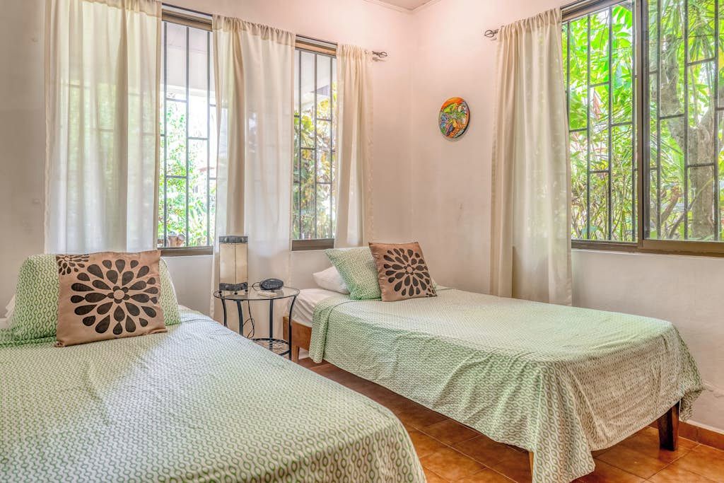 A room with two beds, a small table, and a window with curtains.