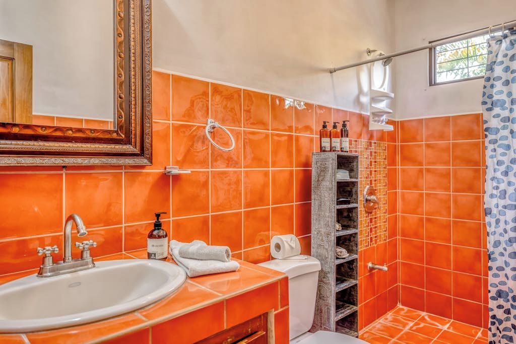 A bathroom with orange tiles, a white sink, a mirror, and a shower area.