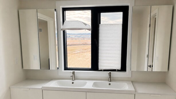 Ein Badezimmer mit einem Doppelwaschbecken, einem Fenster mit Blick auf ein Feld und einem Spiegel über dem Waschbecken.