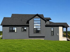 A modern two-story house with a flat roof, large windows, and a visible chimney.