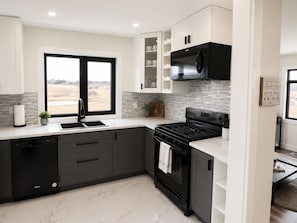 A modern kitchen with a black stove, white cabinets, and a window with a view of the outdoors.