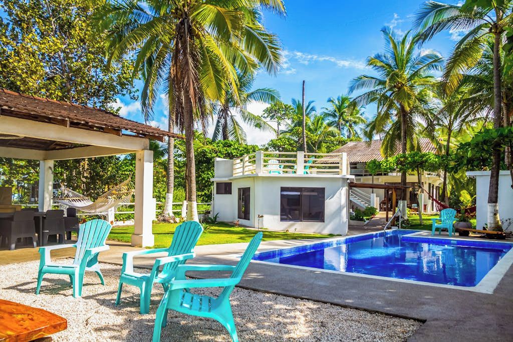 Un área de piscina con sillas, un edificio pequeño y palmeras.