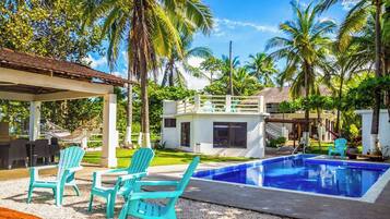 Un área de piscina con sillas, un edificio pequeño y palmeras.