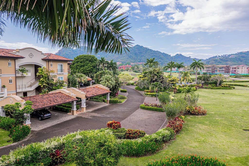 A hotel with a paved driveway, covered parking, and lush landscaping.