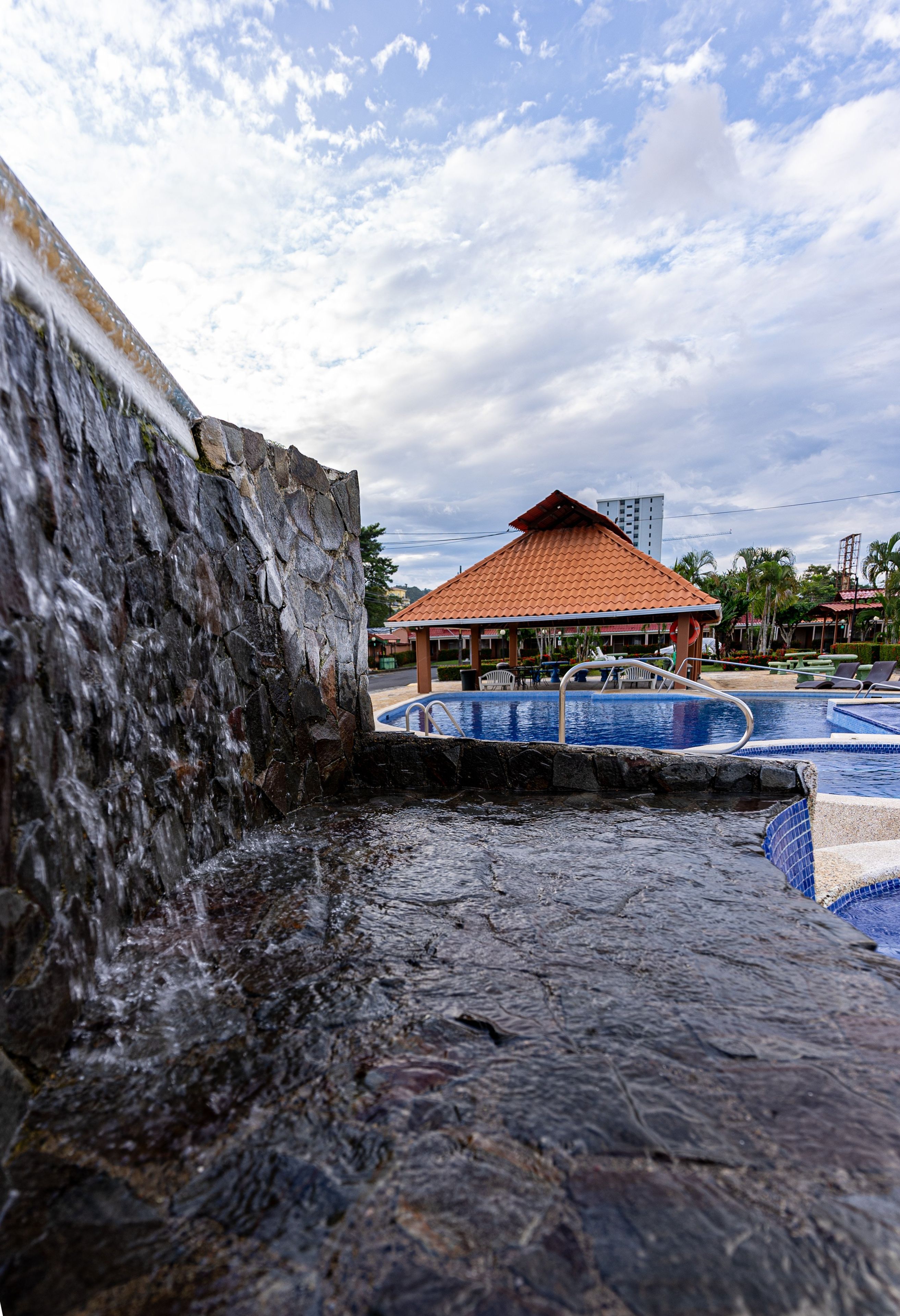 A stone water feature with a pool and a pavilion in the background.